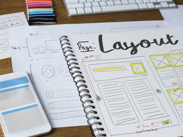 Notizbuch mit Layout-Skizze, Smartphone und Tastatur